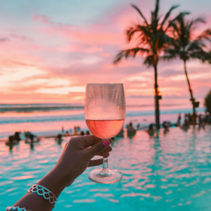 Une main tenant un verre de vin devant la piscine au coucher du soleil à Bali, en Indonésie.