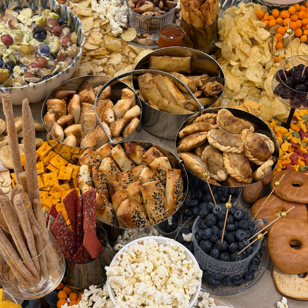 Une abondante variété d'amuse-gueules et de collations, incluant du pop-corn, des chips, des pâtisseries, des empanadas, une salade de fruits, des myrtilles, des fraises et des grissinis.