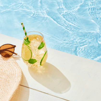 un chapeau, des lunettes de soleil et une boisson au bord de la piscine